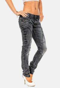 Jeans in denim grigio con vestibilità slim, caratterizzati da cuciture bianche, una tasca con zip e un design di pannelli distintivi. Indossati con scarpe con tacco a pianta bianca.