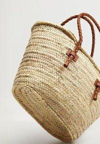Geweven rieten tas met een ronde vorm, bruine gevlochten leren handvatten en leren accenten aan de zijkanten, met een natuurlijke, gestructureerde afwerking.