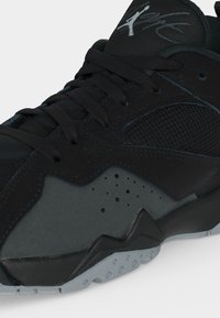 Chaussure de sport noire et gris foncé avec lacets, détail perforé sur le côté, panneau en mesh et un logo sur la languette.