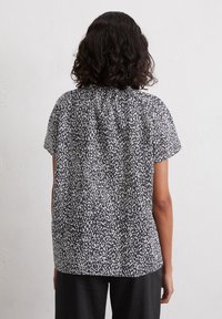 Short-sleeved black blouse with a white speckled pattern, featuring a gathered neckline and a relaxed fit, made from lightweight fabric.