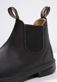 Botín Chelsea de cuero negro con panel lateral elástico, tira de agarre, acabado texturizado y suela de goma duradera. Diseño clásico de altura de tobillo.