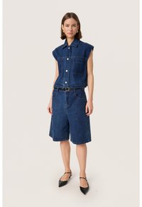 Denim majica bez rukava s zatvaranjem na gumb i dva prednja džepa, u kombinaciji s trapericama do koljena. Tamnoplava boja, glatka tekstura.