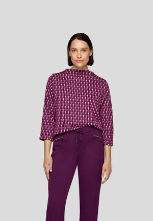 Purple patterned blouse with geometric design and 3/4 sleeves, paired with dark purple pants featuring zippered pockets and a drawstring waist.