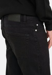 Czarne dżinsy z denimu o fakturowanej tkaninie, dopasowanym kroju, tylną kieszenią ze szwem oraz skórzaną metką marki na pasku.