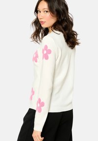 White knit sweater featuring large pink flower patterns, round neckline, and long sleeves. Soft texture with a fitted silhouette.