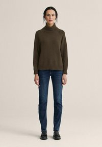 Brun rullekrave sweater med ribbede manchetter, kombineret med mørkeblå jeans og sorte sko. Enkel design med en afslappet pasform og tekstureret stof.