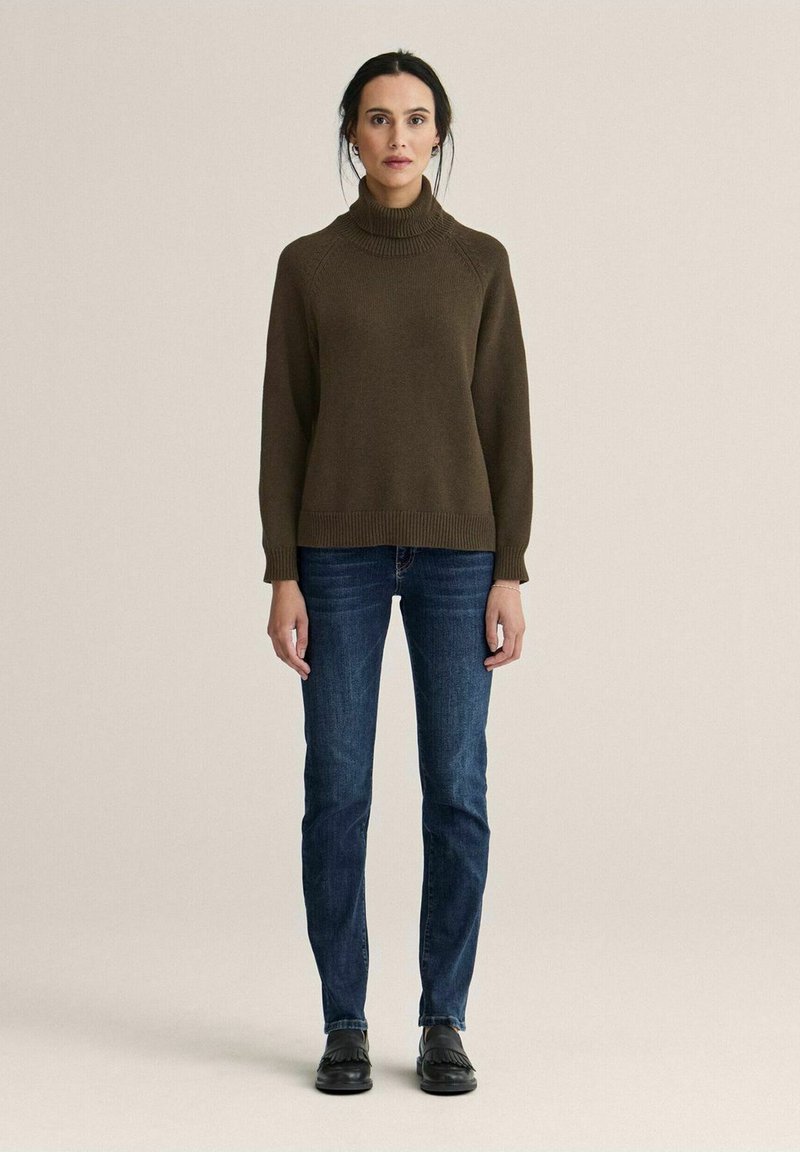 Brun rullekrave sweater med ribbede manchetter, kombineret med mørkeblå jeans og sorte sko. Enkel design med en afslappet pasform og tekstureret stof.