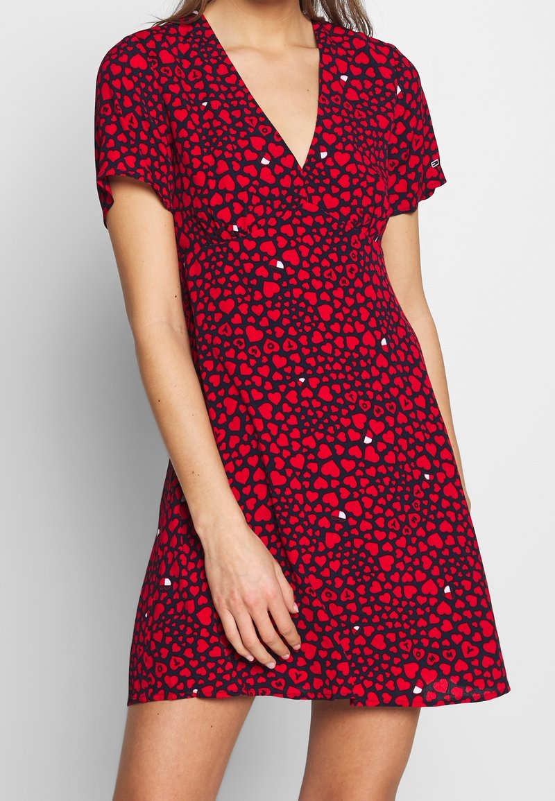 Vestido rojo con escote en V, mangas cortas, hecho de una tela suave, con un estampado de pequeños corazones sobre un fondo oscuro.