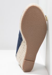 Semelle d'une espadrille compensée avec un fond texturé de couleur tan, une plateforme en jute tressé naturel et une tige en tissu bleu marine, affichant la taille 4.