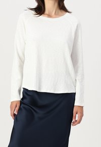 Top bianco a maniche lunghe con scollatura rotonda e maniche raglan, abbinato a una gonna di raso blu scuro. Tessuto morbido, vestibilità casual.
