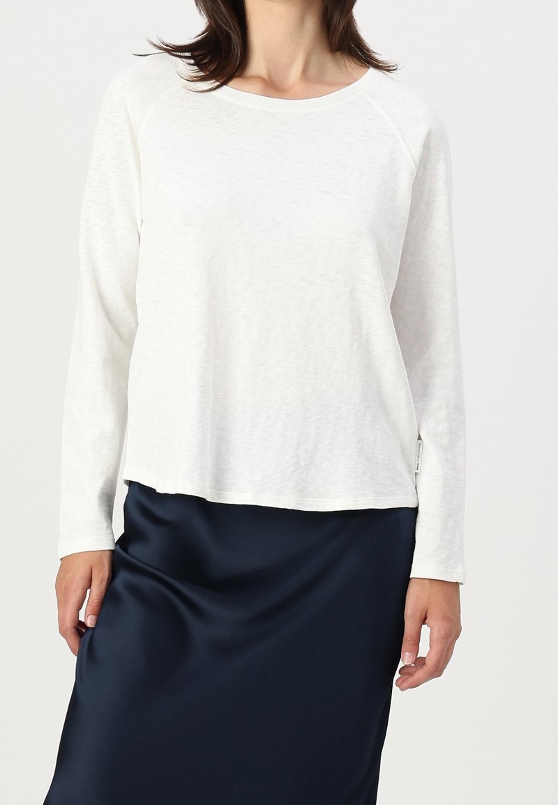 Top bianco a maniche lunghe con scollatura rotonda e maniche raglan, abbinato a una gonna di raso blu scuro. Tessuto morbido, vestibilità casual.