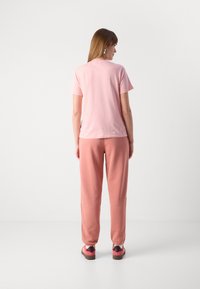 T-shirt di cotone rosa e pantaloni della tuta abbinati. Texture morbida, taglio rilassato, design semplice e polsini elastici sui pantaloni. Calzature casual in rosa e marrone.