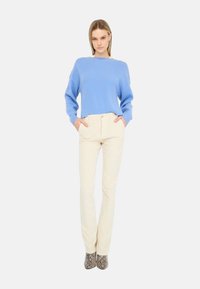 Maglione azzurro chiaro con scollo ampio, abbinato a pantaloni aderenti color crema e stivali grigi con stampa a motivo serpente testurizzata.