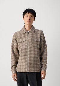 Chaqueta de cuadros marrones con cremallera, dos bolsillos frontales, cuello amplio y mangas largas, con una tela texturizada y un corte ajustado.