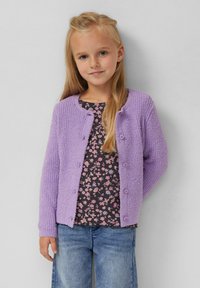 Lavendelkleurige gebreide cardigan met textuurstof, ronde halslijn en knoopsluitingen, gedragen over een donker bloemenpatroon top en blauwe jeans.