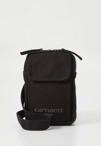 Liten svart skulderveske med frontlomme med klaff, glidelås på toppen og matchende justerbar stropp, merket "Carhartt WIP" i grått.