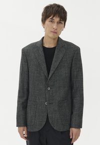 Meeste kohandatud bleiser tumesinises tekstuurses kangas. Omab ühte nupuvajutust, krae ja kahte esist taskut.