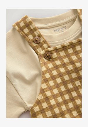 Rjavi in kremasti karirani kombinezon z detajli gumbov, v kombinaciji s preprosto kremasto majico. Gladek material z lahkotno teksturo.