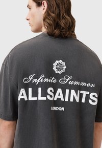 T-shirt oversize gris foncé avec texte imprimé blanc "Infinite Summer ALLSAINTS LONDON" au dos, en coton doux, coupe décontractée.