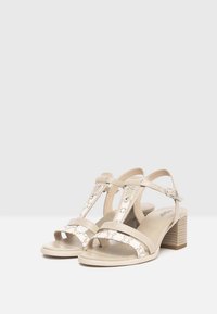 Beige high-heeled sandals with a combination of smooth leather and patterned straps. Feature adjustable ankle strap and a block heel.