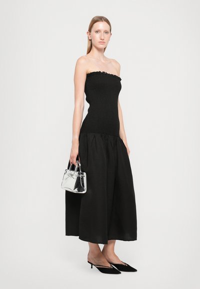 Zwarte strapless top met een textuur gebreide stof en een gehaalde onderrand, gecombineerd met een zwarte vloeiende rok, een doorzichtige handtas en zwarte puntige kittenhakken.