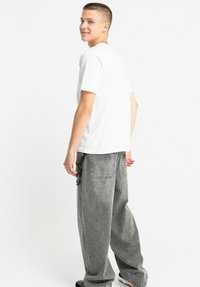 Biała koszulka z krótkim rękawem w połączeniu z luźnymi, jasnoszarymi spodniami dżinsowymi. Strój charakteryzuje się swobodną sylwetką z subtelną fakturą.