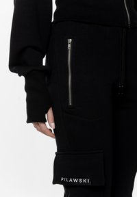Czarny zestaw bluz i spodni wykonany z miękkiej tkaniny. Posiada kieszeń na zamek, ściągacze przy mankietach oraz logo "PILAWSKI" na nogawce.