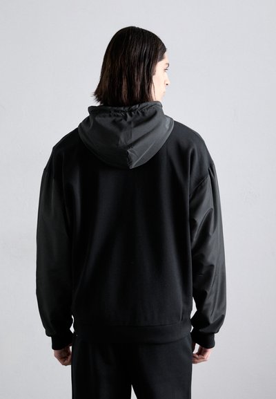 Schwarzer Hoodie mit einer glatten Textur, oversized Passform und einer kontrastierenden Kapuze. Das Design umfasst gerippte Bündchen und einen Saum.