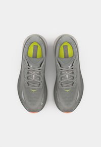 Scarpe da corsa grigie con una tomaia texturizzata, caratterizzate da un accento giallo brillante sulla linguetta e un dettaglio arancione vicino alla suola.