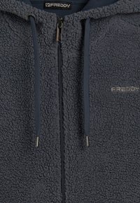 Sudadera con cremallera forrada de forro polar en gris oscuro, con una textura suave, capucha con cordón y elementos metálicos plateados en la cremallera. Logo bordado visible.