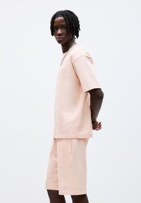 Set de tricou și pantaloni scurți din bumbac roz, cu croială lejeră, detalii logo discrete, guler rotund și buzunare laterale pentru funcționalitate și confort.
