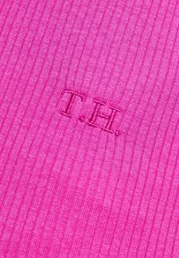 Hladce pletená látka v jasně růžové barvě s vyšitým logem "T.H." v mírně tmavší růžové, která se vyznačuje jemnou texturou a rovnoměrným vzorem.