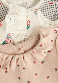 Trys megztiniai iš minkštų medžiagų: rožinė ruffles palaidinė su gėlių akcentais, balta gėlių rašto dalis ir languotas dizainas.