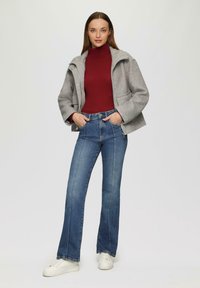Harmaa villasekoitekietunnus, jossa on laskostettu kaulus, yhdistettynä istuvaan burgundinpunaisiin turtleneck-paitaan, sinisiin levenneisiin farkkuihin ja valkoisiin tennareihin.