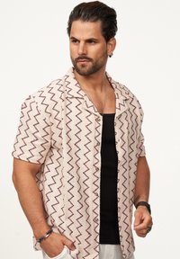 Kurzärmliges Button-Up-Hemd in hellbeige mit einem Zickzackmuster in Dunkelrot. Hat einen entspannten Kragen und einen strukturierten Stoff.