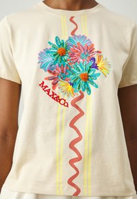 Camiseta de algodón marrón claro con bordado floral colorido, texto rojo "MAX&Co." y acentos en zigzag y rayas en rojo y amarillo.