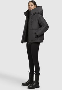 Giacca a vento nera con colletto alto, tasche con zip e maniche larghe. Abbinata a leggings neri e stivali neri chunky.
