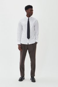 Witte blouse met lange mouwen en een button-down kraag, gecombineerd met bruine op maat gemaakte broek en zwarte dresschoenen; beschikt over een marineblauwe stropdas.
