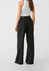 Pantalon large noir à taille haute, avec une texture lisse, deux poches arrière et un design ajusté.