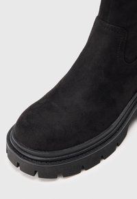 Μαύρο καστόρινο μποτάκι αστραγάλου με στρογγυλεμένη μύτη, παχύ μαύρο καουτσούκ σόλα με αυλακώσεις και διακρ�ιτικές ραφές κατά μήκος των ραφών.