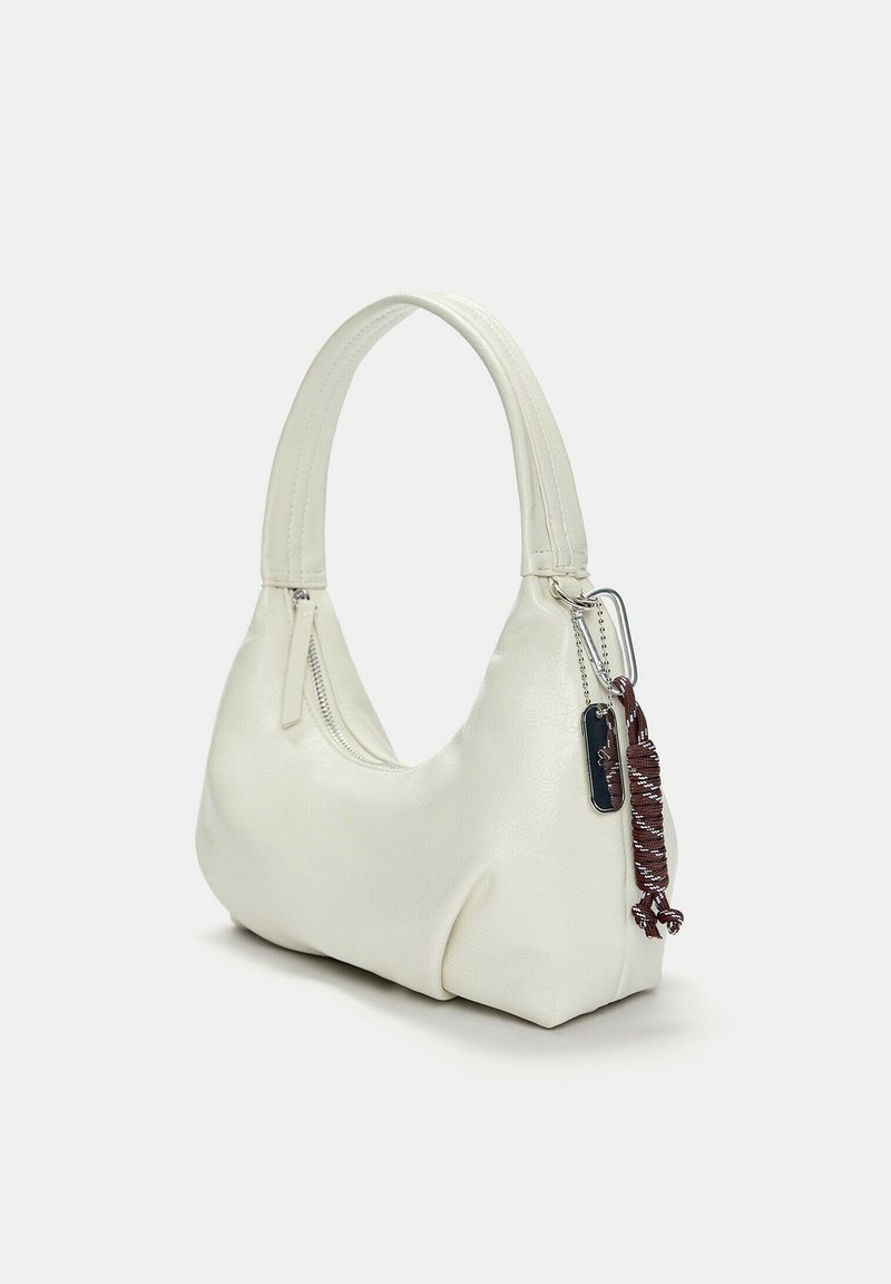 Bolso de mano de cuero sintético blanco con forma curva, cierre de cremallera y una correa corta para el hombro. Presenta un fleco decorativo y una etiqueta.