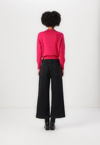 Fuksia genser med ribbestrikket kant og dekorative nagler, kombinert med vide svarte denimbukser og chunky helte støvler.