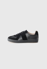 Baskets noires en cuir et en daim, dotées d'une semelle en caoutchouc texturé gris, d'un bout rond et de lacets noirs. Design minimaliste avec des accents.