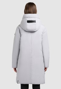 Šviesiai pilka pūkinė striukė su aukštu apykakliu ir firminiu ženklu nugaroje. Turi ilgus rankogalius ir šiek tiek siaurėjantį siluetą.