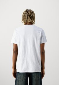 T-shirt de algodão branca com mangas curtas, design de gola redonda e textura suave. Usada com calções de ganga escuros, com bolsos traseiros.