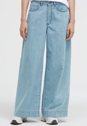Light blue wide-leg jeans with thin white vertical stripes worn with white sneakers and a tucked-in white shirt.