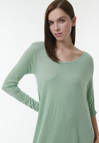 Blusa de manga larga en verde menta, hecha de un tejido ligero con un corte holgado, que presenta un escote amplio y mangas ligeramente ajustadas.
