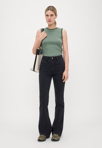 Top sin mangas a rayas verdes, jeans negros de talle alto y acampanados, bolsa de lona, y zapatillas verde oliva. Conjunto simple y casual.