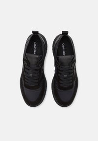 Černé sportovní boty s kombinací hladkých a texturovaných materiálů, šněrovacím designem, zaoblenou špičkou a drážkovou gumovou podrážkou.