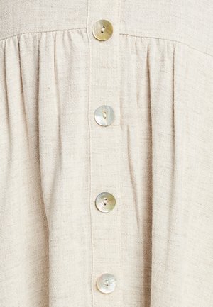 Gaišs bežs lina audums ar pogu aizdari, kas satur piecas apaļas, mirdzošas pogas. Materiāls ir teksturēts, ar nedaudz salocītu izskatu.